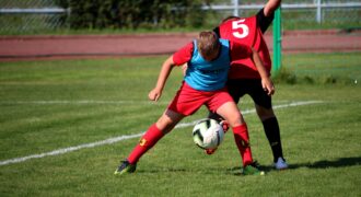 Doi copii jucând fotbal pe teren.