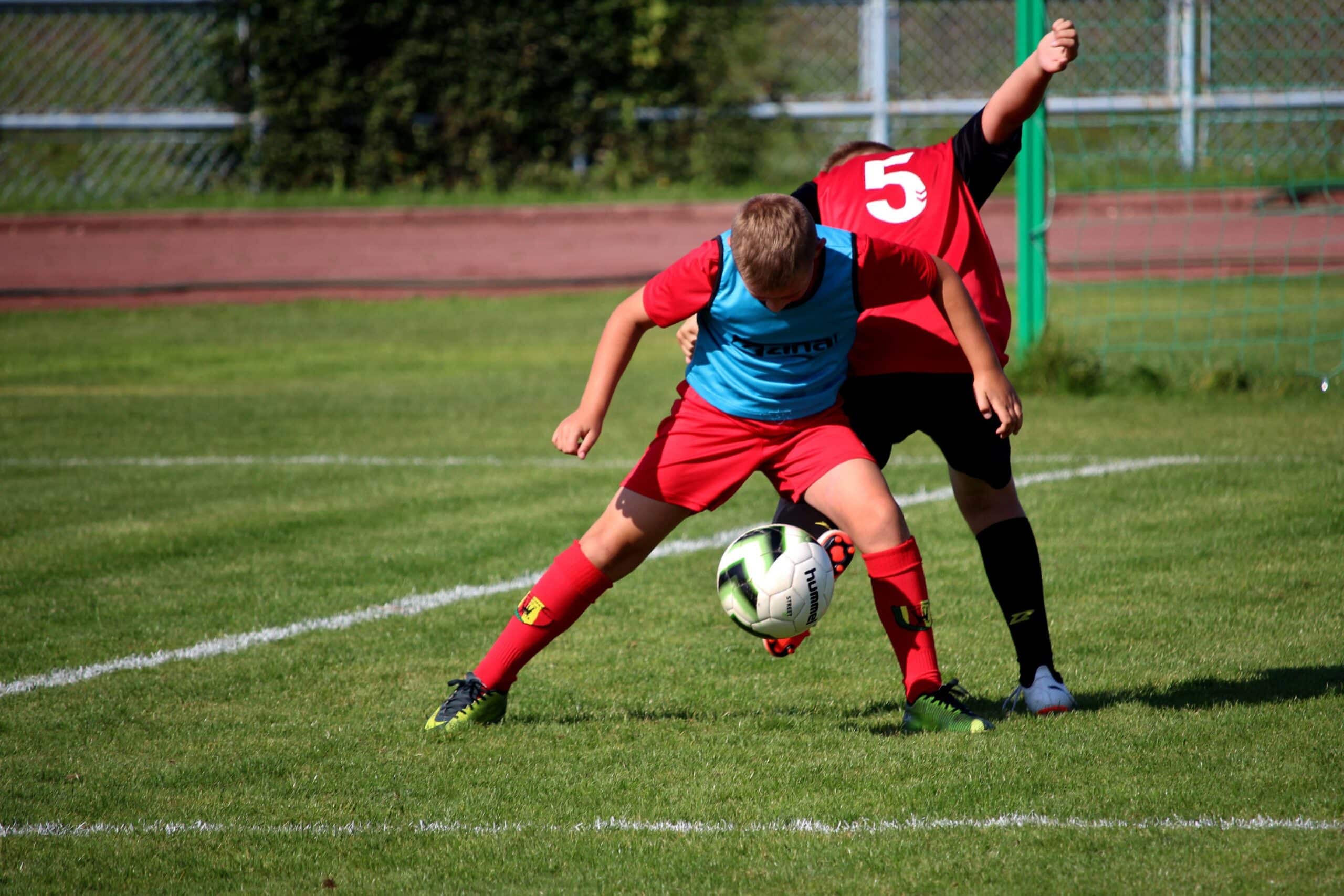 Doi copii jucând fotbal pe teren.